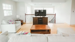 Een ruime woonkamer met een witte zithoek, een houten salontafel en een flatscreen televisie op een houten kast.
