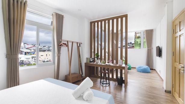 Habitación de hotel con cama, escritorio, silla, separador de madera y vista de la ciudad.
