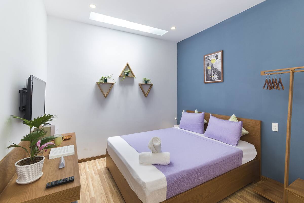A modern bedroom with a bed, bedside table, potted plant, and a painting on the wall.