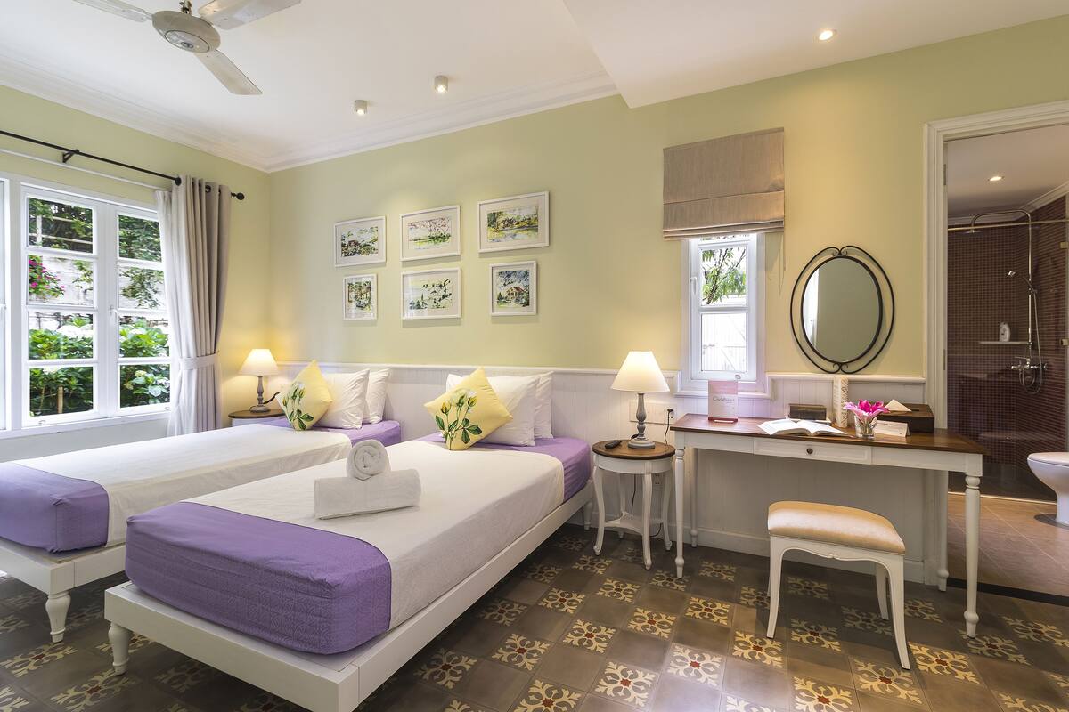 Ein Hotelzimmer mit zwei Betten, einem Schreibtisch, einem Stuhl, einer Dusche und Kunstwerken an den Wänden.