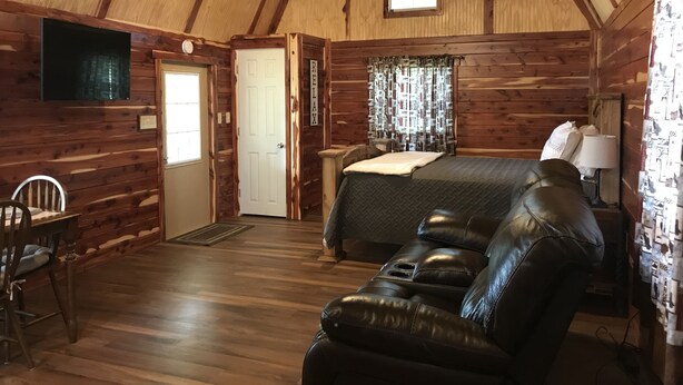 Un accogliente interno di una baita con arredamento in legno, un letto, un divano in pelle e un televisore.