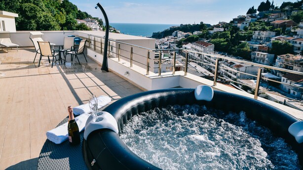 Une terrasse sur le toit avec un jacuzzi, des chaises longues et une table sur laquelle est posée une bouteille de champagne.