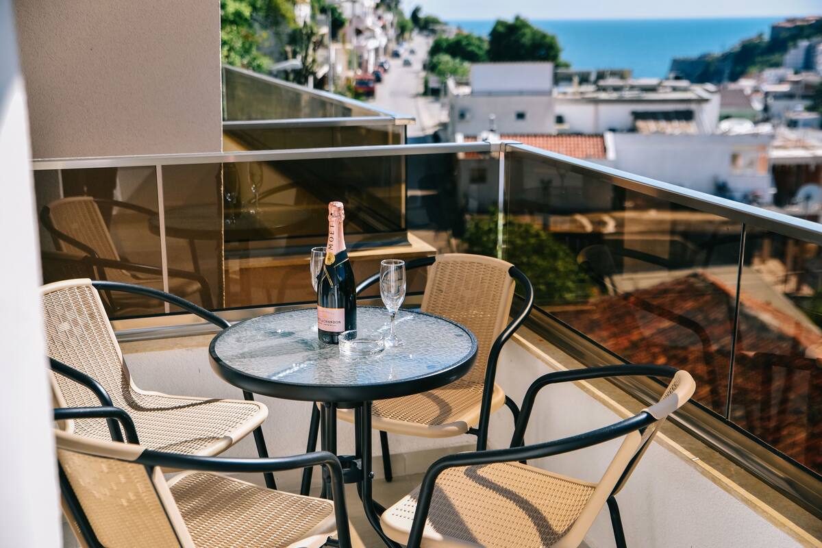 A balcony with a table, chairs, a bottle of champagne, and glasses.