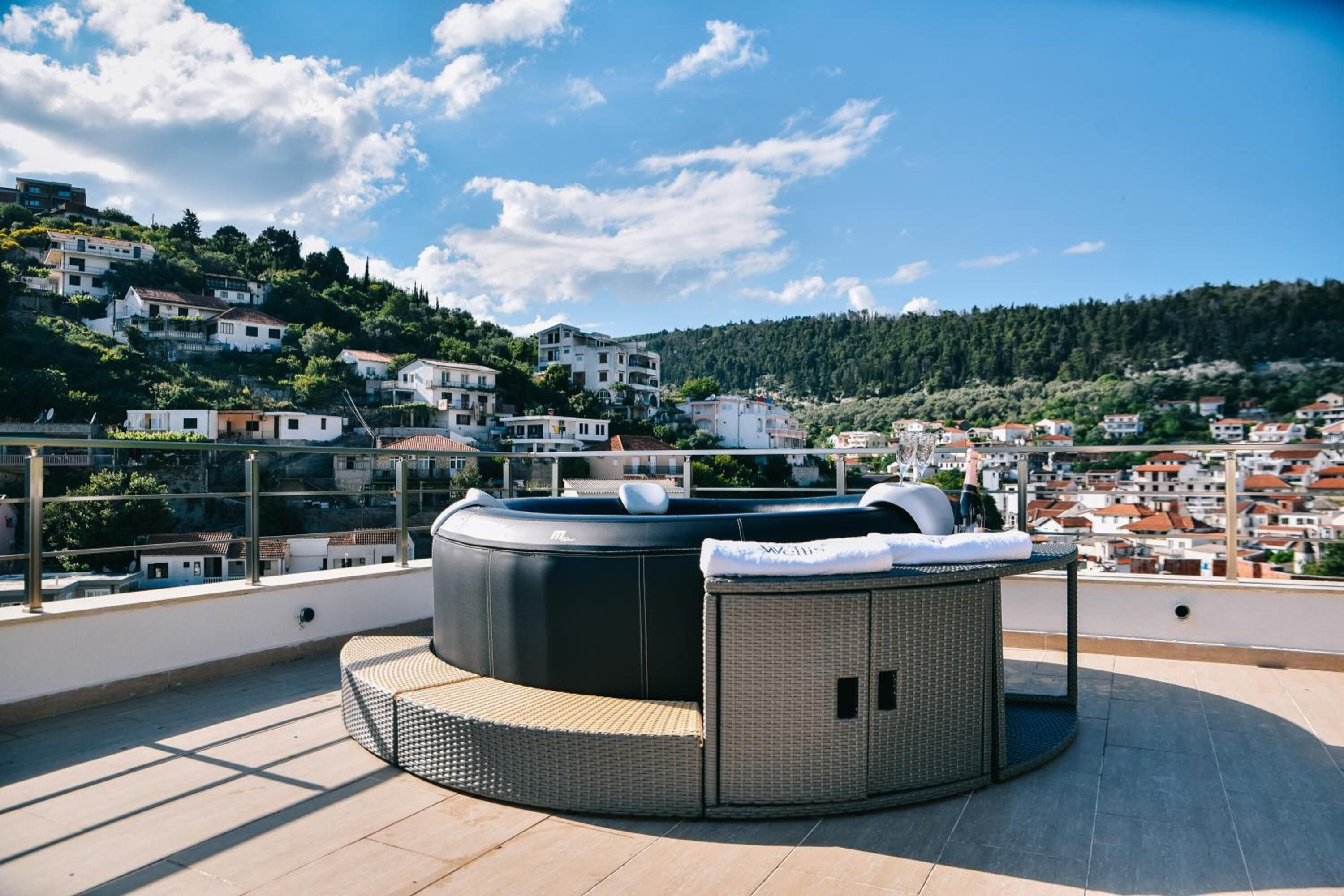 Una terraza en la azotea con un jacuzzi, una zona de estar de mimbre y vistas a un pueblo en la ladera.