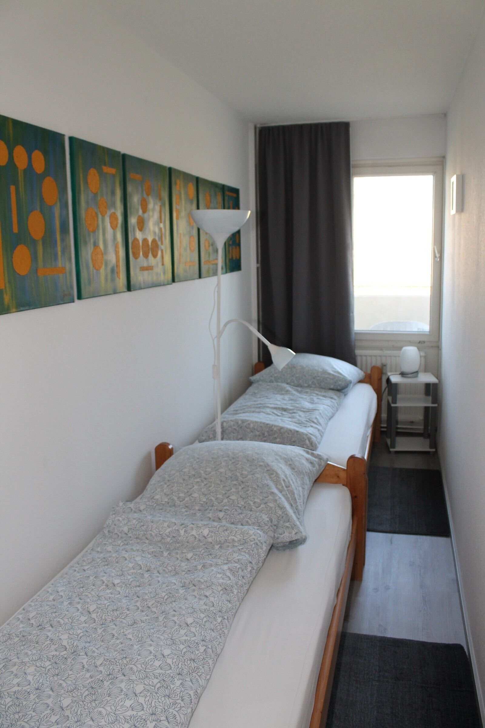 Ein Hotelzimmer mit zwei Einzelbetten, einem Nachttisch, einer Lampe und einem Fenster mit Vorhängen.