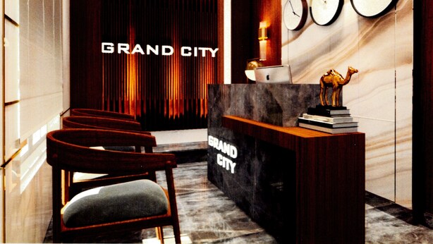 A reception area with a dark curtain backdrop, a reception desk, a chair, and three clocks on the wall. - Grand City Hotel (Cairo)
