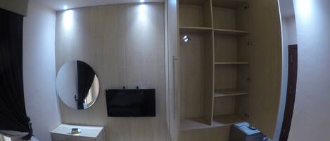 A modern bedroom with a built-in wardrobe, a TV mounted on the wall, and a bedside table.