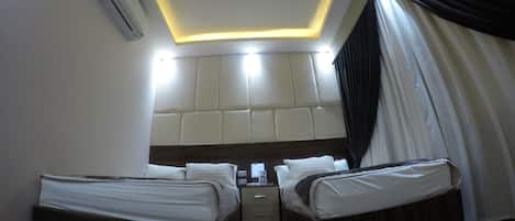 A hotel room with two beds, a wooden floor, a headboard with a padded back, and an air conditioning unit.