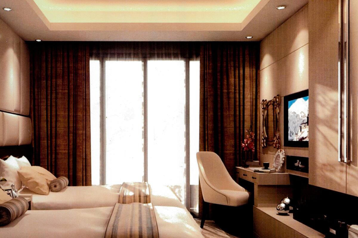 Una habitación de hotel con dos camas, un escritorio, una silla, un televisor y un ventanal grande con cortinas.