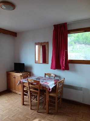 A room with a wooden table, chairs, a television on a cabinet, a mirror, and a window with red curtains. - Wifi, 3rd floor, swimming pool, balcony, parking, tv, ski locker, 25m², Puy-Saint-Vincent (Puy-Saint-Vincent)