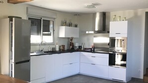 Moderni keittiö, jossa on valkoiset kaapit, ruostumattomasta teräksestä valmistetut kodinkoneet ja puinen katto.