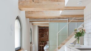 Una cocina moderna con armarios blancos, piso de madera y una escalera de vidrio que conduce a un comedor.