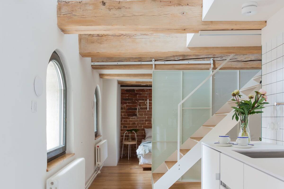 A modern kitchen with white cabinetry, a wooden floor, and a glass staircase leading to a dining area.