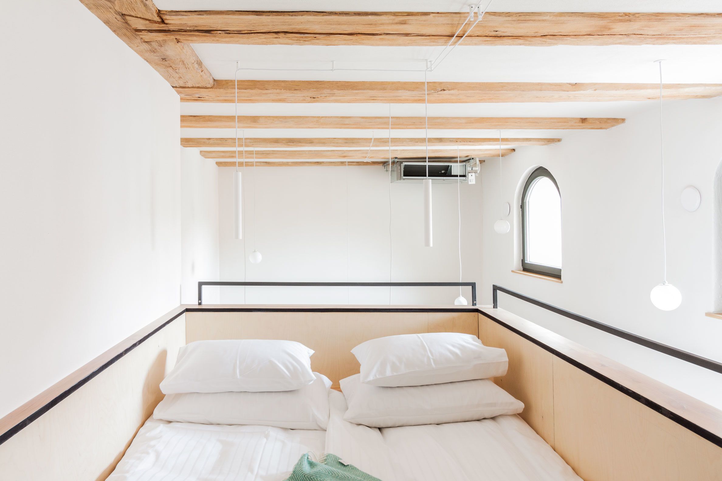 Een slaapkamer met een houten plafond, een bed met wit beddengoed, een raam en een aan de muur bevestigde airconditioning.