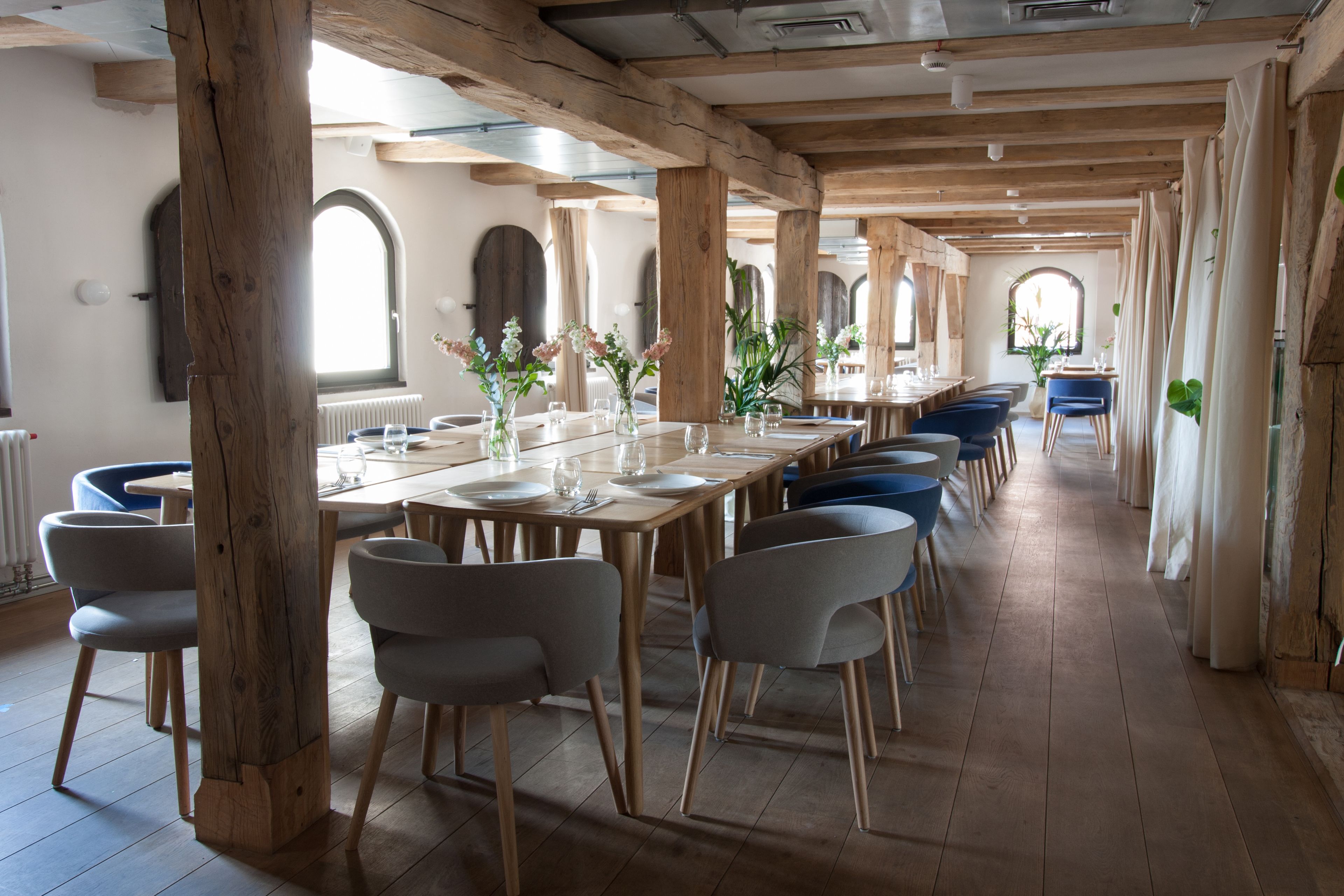 Una larga mesa de comedor con sillas, vigas de madera y ventanas amplias.