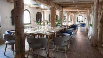 Una larga mesa de comedor con sillas, vigas de madera y ventanas amplias.