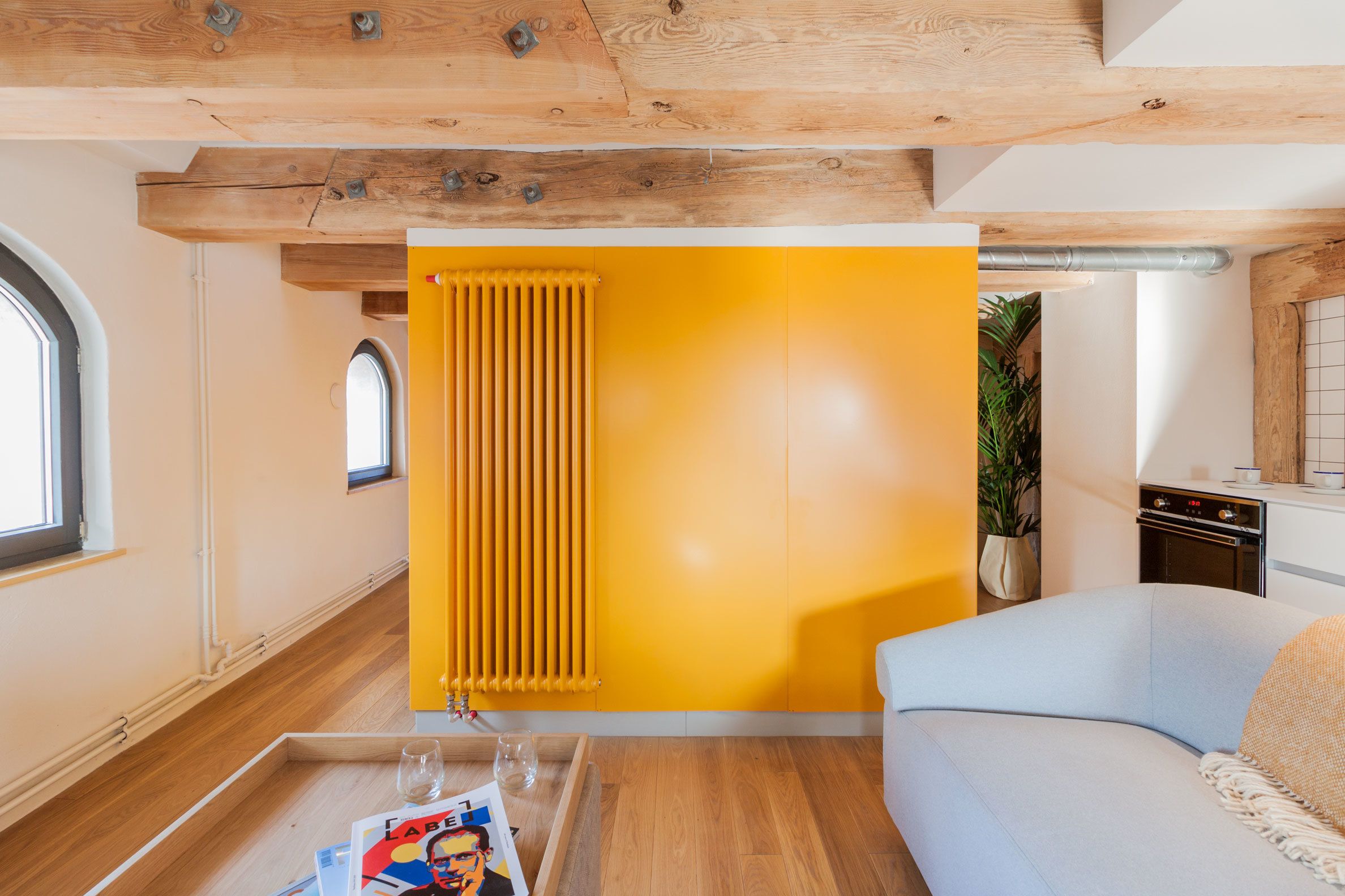 Una sala de estar moderna con techo de madera, un radiador amarillo, un sofá azul claro y una mesa de centro de madera con revistas y vasos.