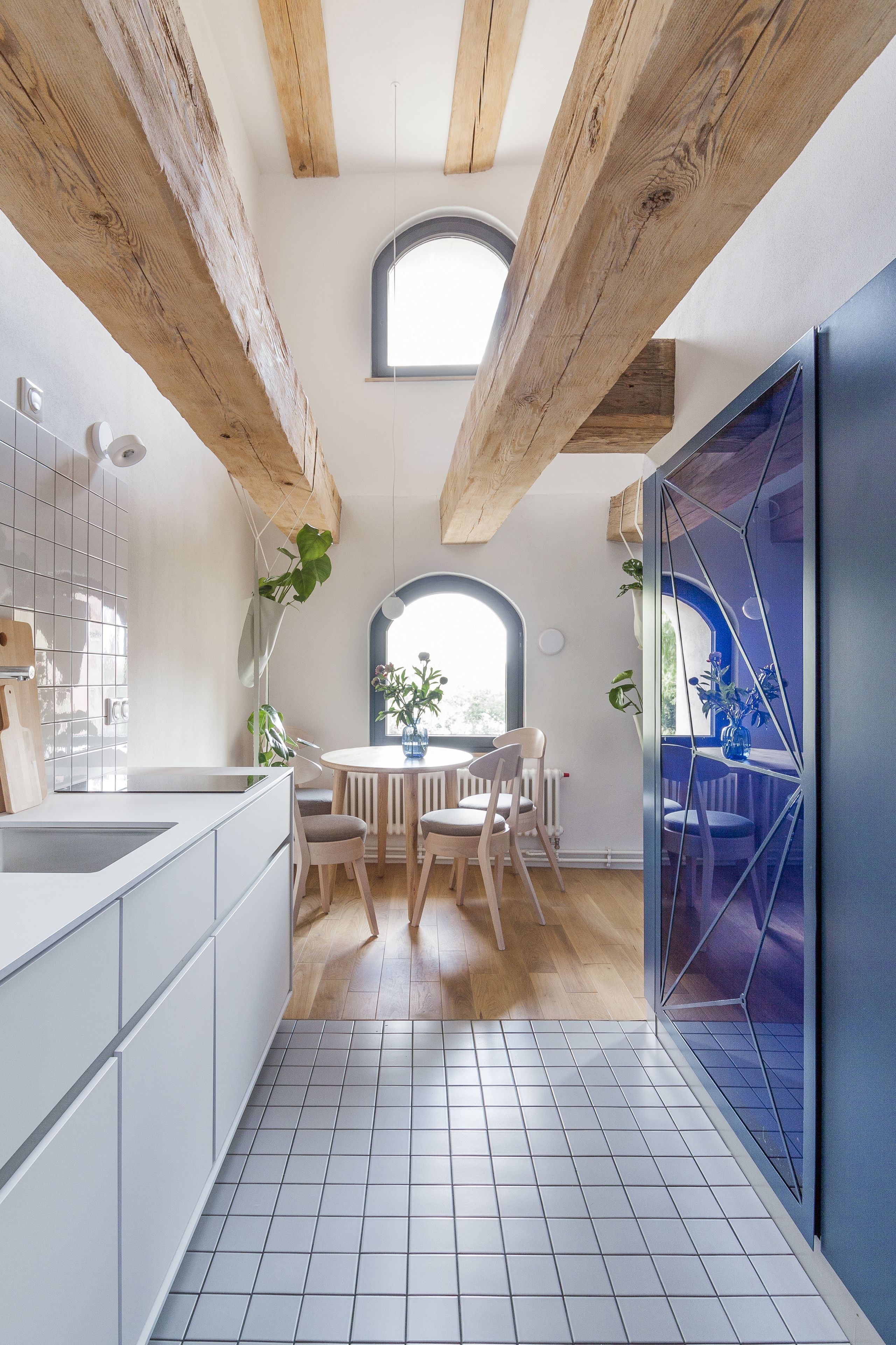 A modern kitchen with white cabinets, a wooden ceiling, and a dining area with a round table and chairs.