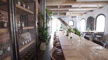A dining area with a long table, chairs, and potted plants.
