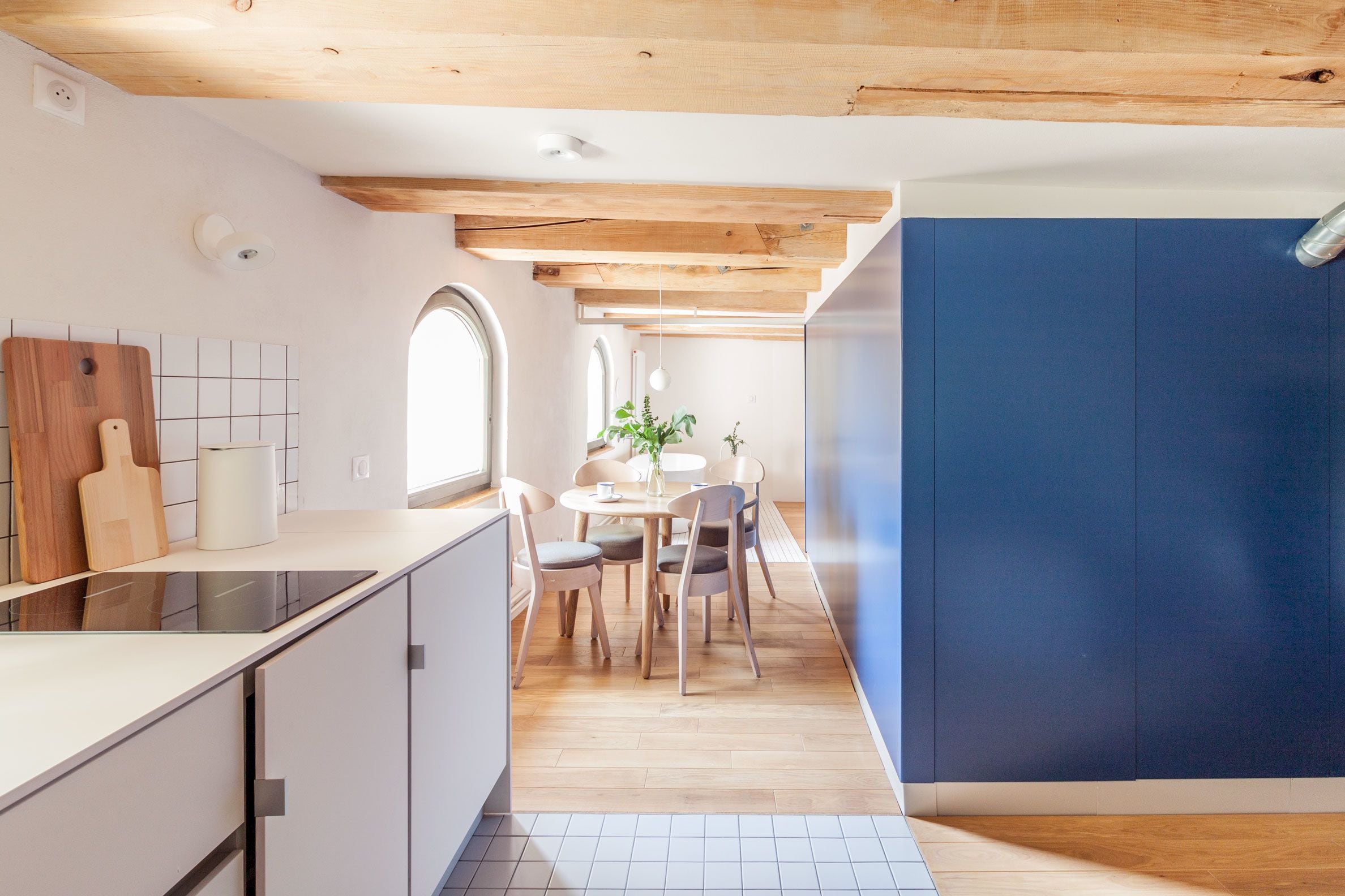 A modern kitchen with a wooden ceiling, a dining area with a round table and chairs, and a large window.