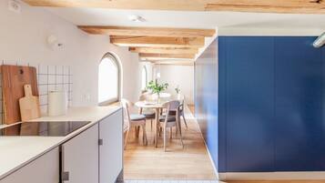 A modern kitchen with a wooden ceiling, a dining area with a round table and chairs, and a large window.