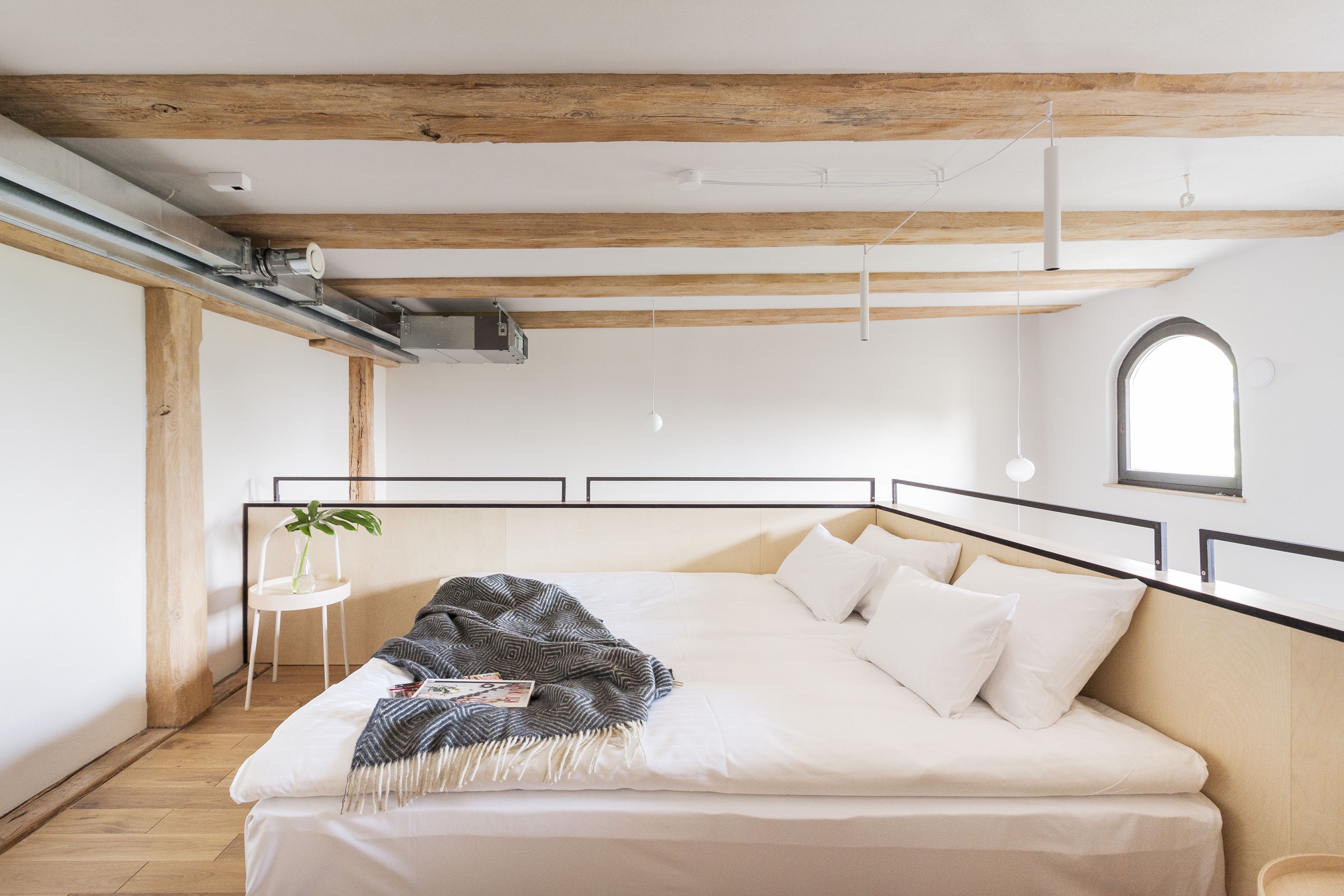 Un dormitorio con una cama grande, vigas de madera, una pequeña silla blanca y una ventana.