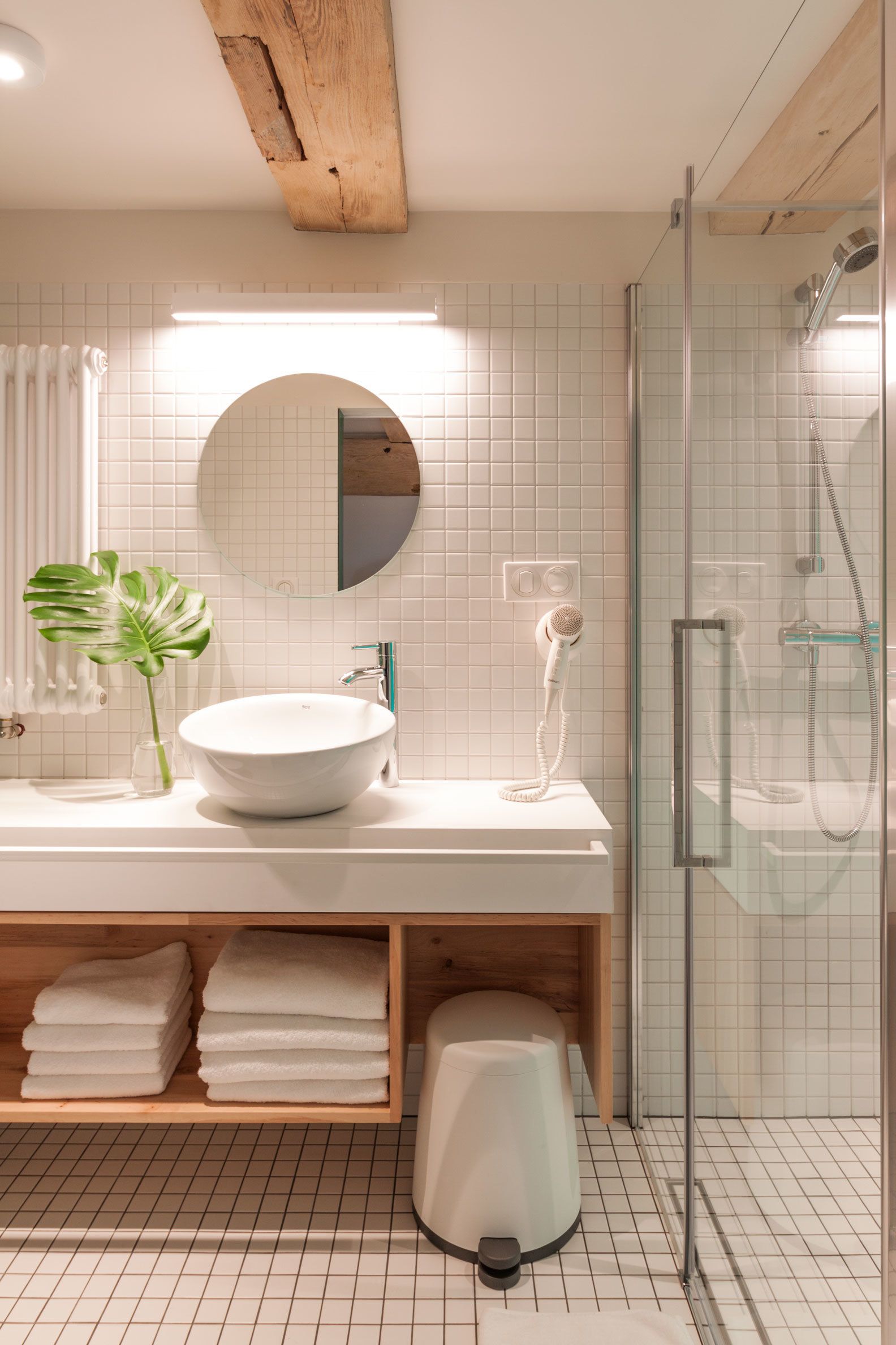 A modern bathroom with a white sink, a round mirror, and a glass shower enclosure.