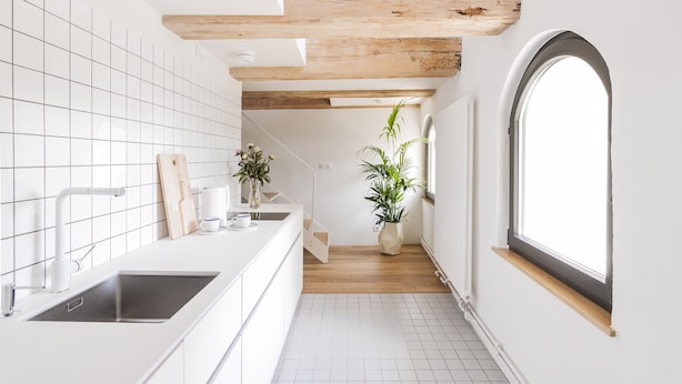 Una cocina moderna con armarios blancos, un lavamanos negro, vigas de madera en el techo y una ventana grande a la derecha.