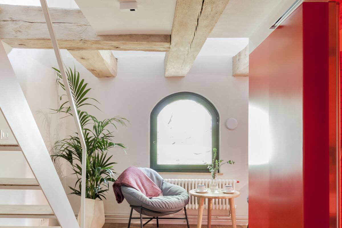 A staircase leading to a room with a wooden floor, a potted plant, a chair, and a window with a view.