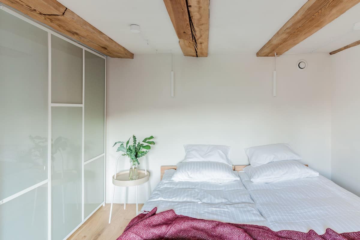 A bedroom with a bed, a bedside table with a plant, and a sliding glass door.
