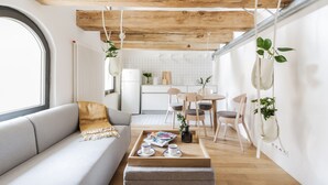 Una sala moderna con techo de madera, un sofá, una mesita de centro con tazas y una revista, y una cocina al fondo.