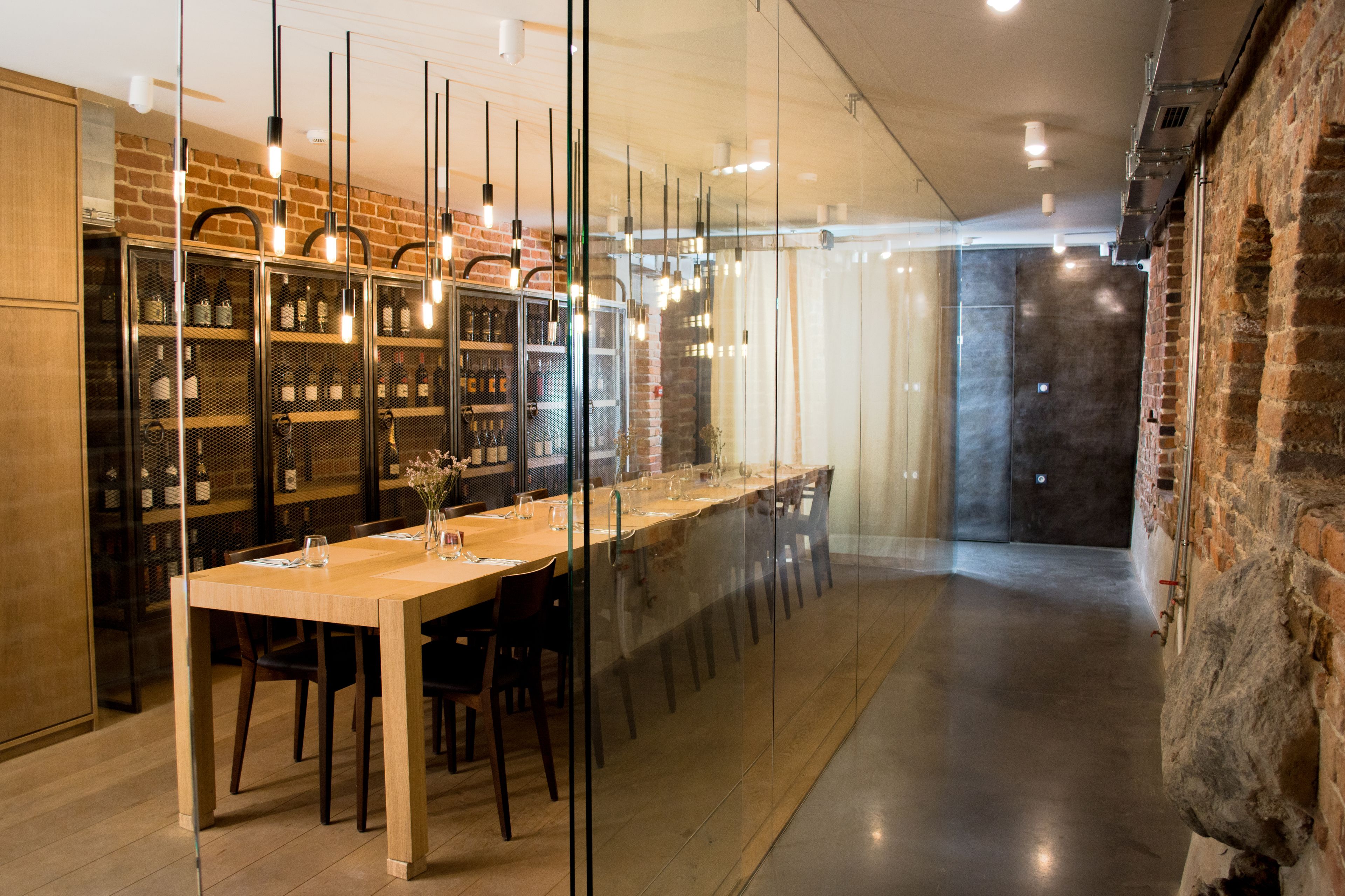 Un espace de salle à manger moderne, avec une longue table, des chaises et un meuble à vin contenant des bouteilles.