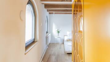 Un pasillo con vigas de madera, una pared amarilla y una cama al fondo.