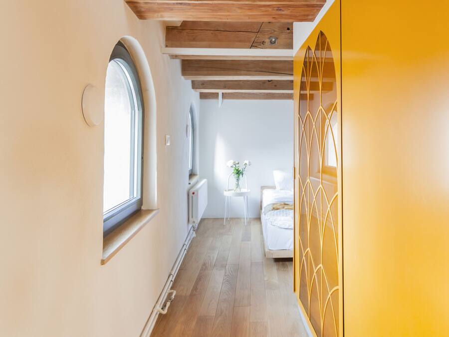 Un pasillo con vigas de madera, una pared amarilla y una cama al fondo.