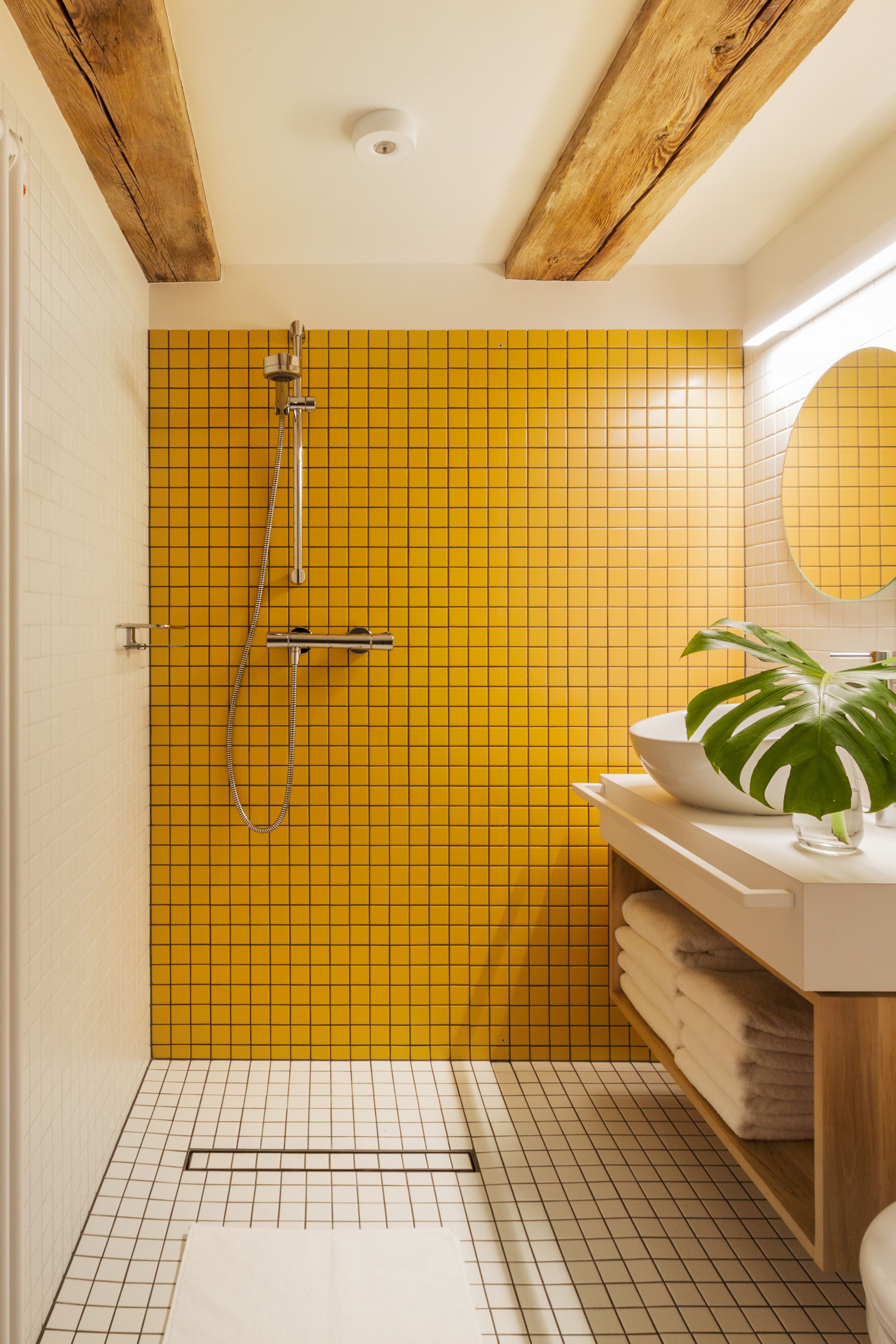 A bathroom with yellow tiled walls, a white sink, a mirror, and a shower.