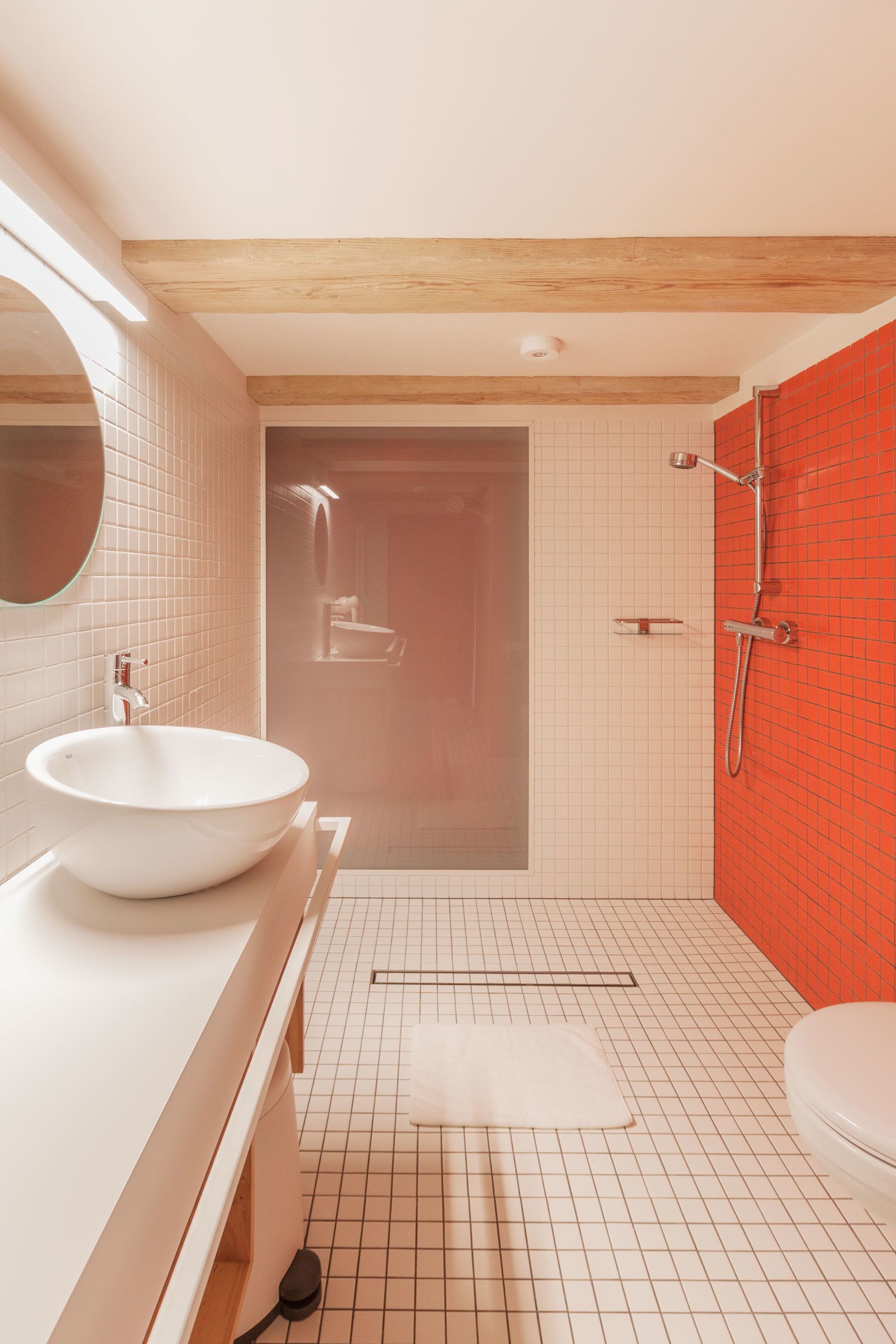 Un baño moderno con un lavamanos grande blanco, un espejo, una ducha con pared de azulejos rojos y un inodoro blanco.