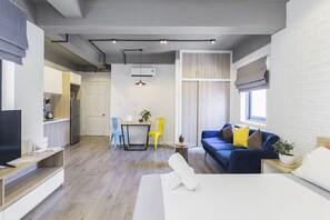 A modern apartment with a living room, dining area, and kitchenette. It features a sofa, a dining table, a TV, and a potted plant.