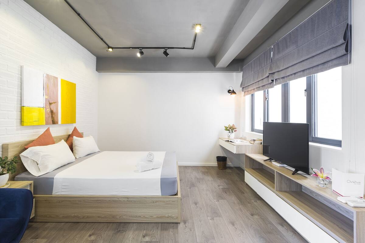 Une chambre moderne avec un lit, une table de chevet, une télévision et une fenêtre avec des stores.