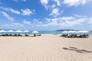 Une plage bordée de rangées de chaises longues et de parasols, un ciel dégagé et l’océan en toile de fond.