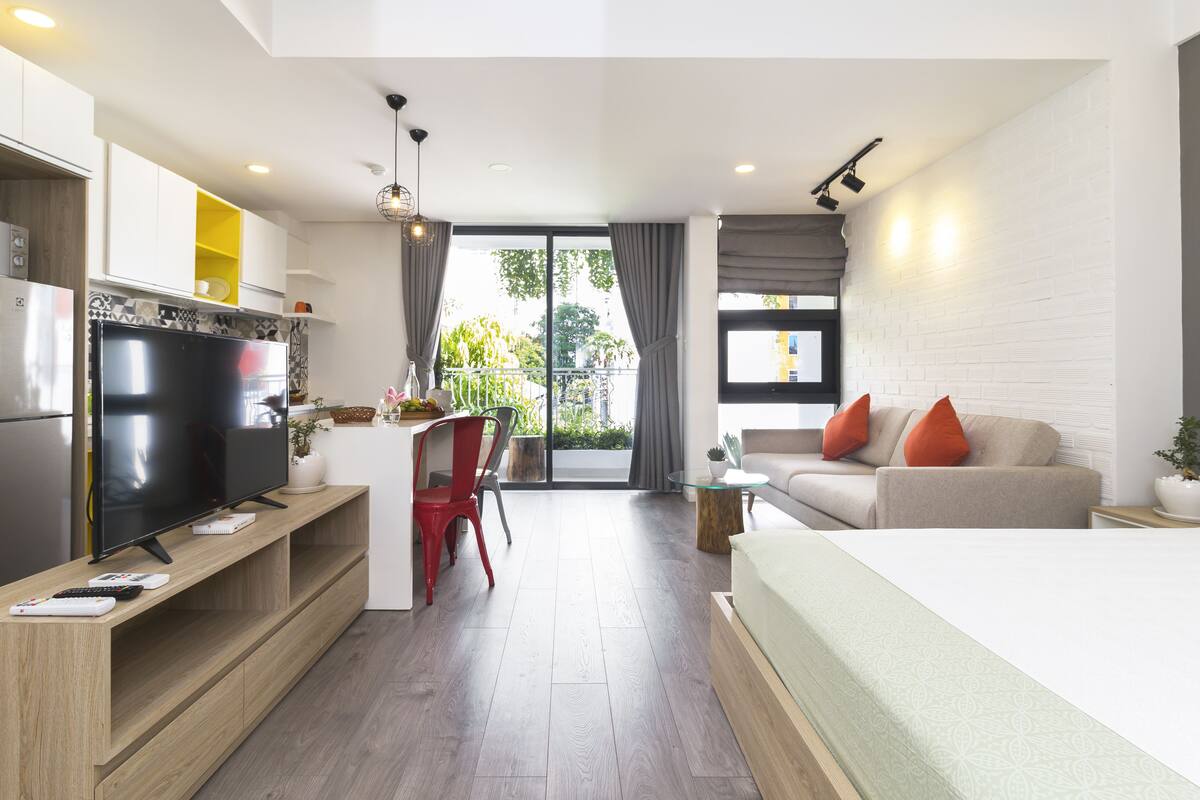 Une chambre d’hôtel moderne dotée d’une télévision à écran plat, d’un canapé, d’un lit, d’un coin repas avec une chaise rouge et d’un balcon avec des rideaux.