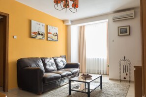 A living room with a black leather sofa, a glass coffee table, and artwork on the walls. - Maxxy Apartments (Bucharest)