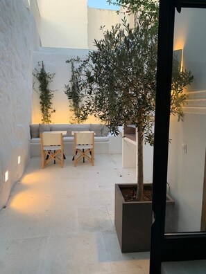 Un área de estar moderna al aire libre con un sofá y dos sillones, un árbol en maceta y un pozo de fuego.