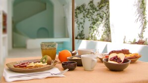 Ein Frühstückstisch mit verschiedenen Speisen, einem Saftglas und einer Tasse unter einem Sonnenschirm.
