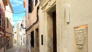 Eine Kopfsteinpflasterstraße, gesäumt von historischen Gebäuden mit traditioneller Architektur, darunter ein Gebäude mit einer Tafel, auf der "CAN ARAYA" steht.