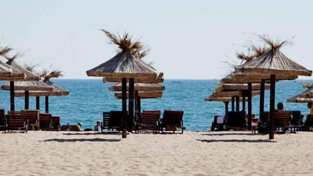 Een strand met houten stoelen en rieten parasols.
