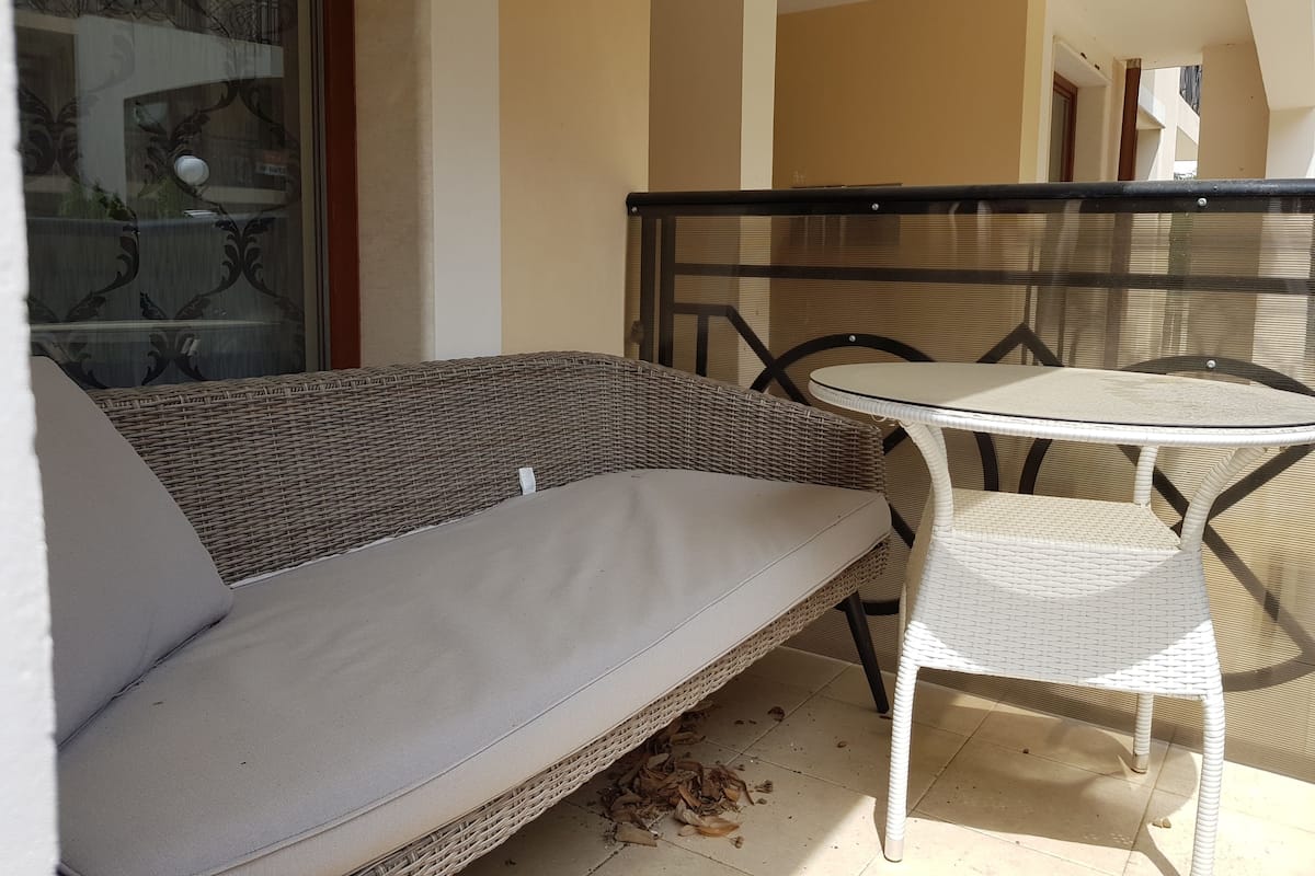 A balcony with wicker furniture, including a sofa and a table, and a glass door with a decorative pattern.