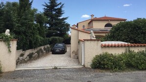 A house with a gravel driveway, a parked car, and a statue on the gate. - 240m2 family villa with swimming pool (Sorede)