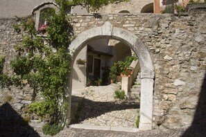 An arched stone doorway leading into a courtyard with a cobblestone path, surrounded by stone walls and potted plants.