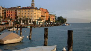 Une promenade en bord de mer avec des bateaux amarrés, une jetée s’avançant dans l’eau et, en arrière-plan, des bâtiments présentant un mélange de styles architecturaux.