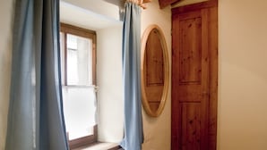 Une chambre à coucher avec un lit, une porte en bois, une fenêtre avec des rideaux et un miroir fixé au mur.